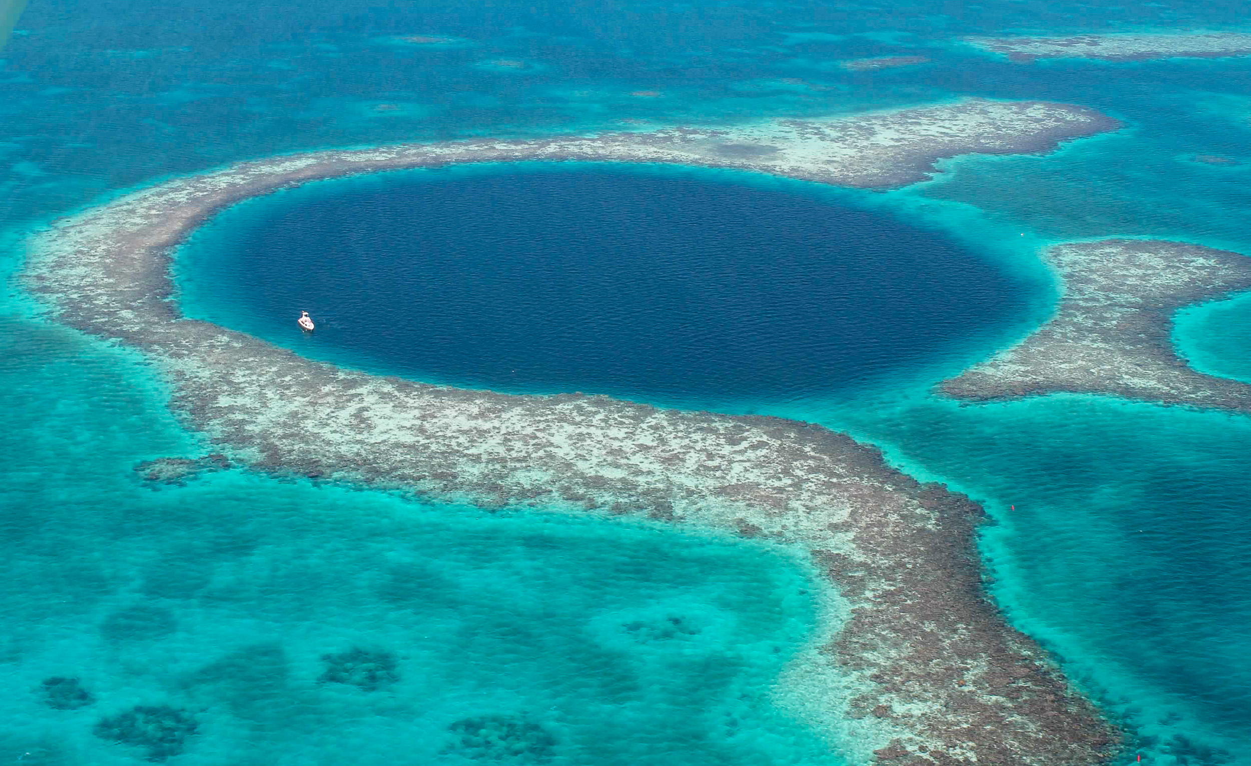 Aerial photograph of the Great Blue Hole surrounded by turquoise coral reefs in Belize.